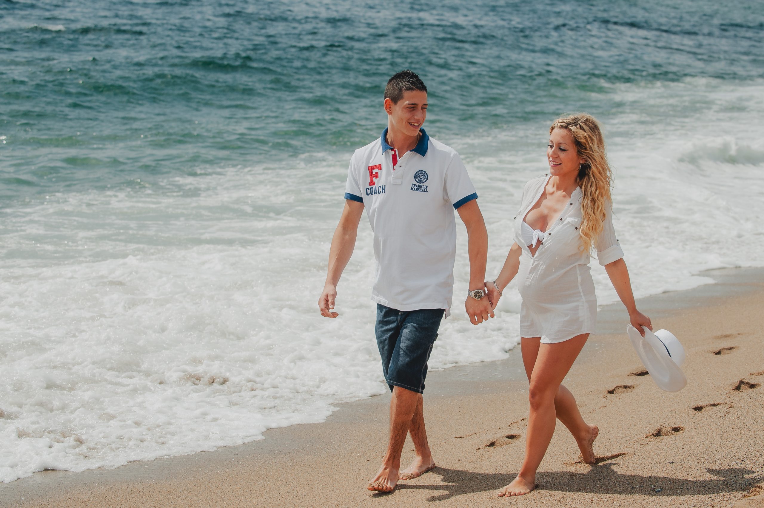 Pareja caminando durante sesión de embarazo en la playa