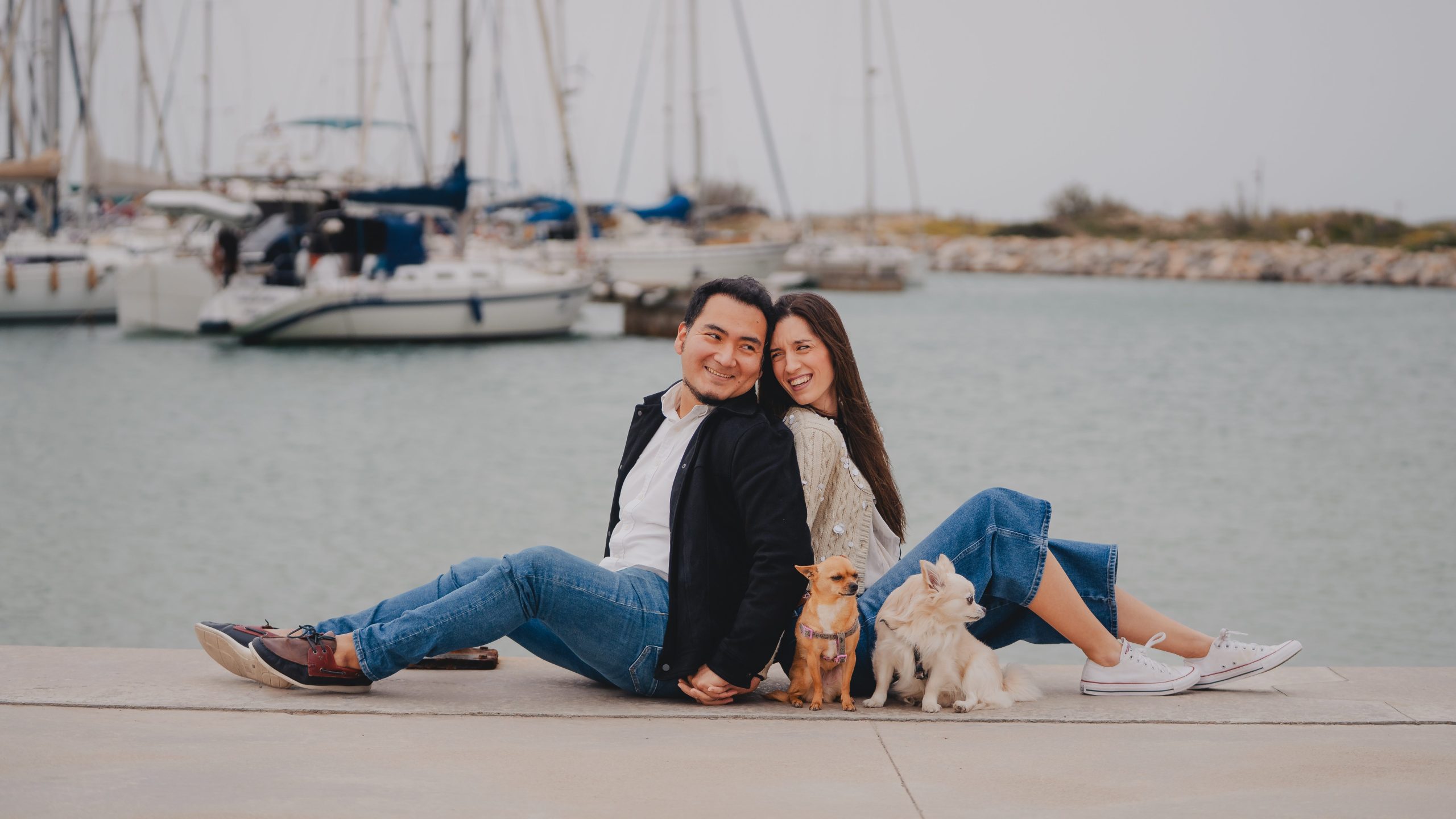 Pareja sentada junto a sus perros durante una sesión de fotos de pareja natural en la costa de Barcelona